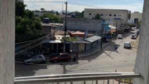 Vista de la calle desde un balcón con baranda de metal. Se ven edificios, coches aparcados y algunas personas en la calle.