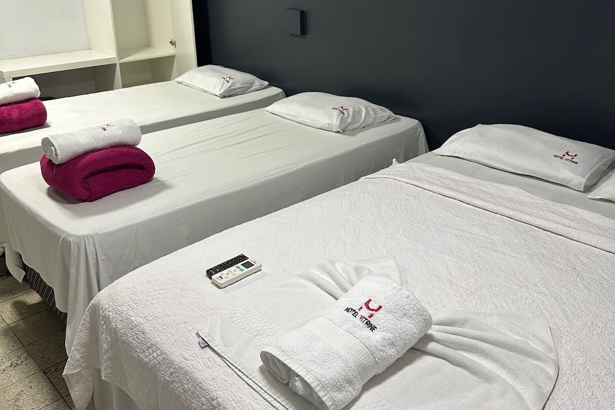 Ein Hotelzimmer mit zwei Betten, jeweils mit weißer Bettdecke und einem Kopfkissen mit dem Hotel-Logo. Auf jedem Bett liegt ein weißes Handtuch, und auf dem linken Bett liegt eine Fernbedienung.