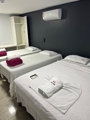 A hotel room with two beds, each with a white bedspread and a pillow with a hotel logo. There is a white towel on each bed, and a remote control on the left bed. - Hotel Vitrine (Goiania)