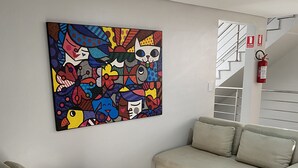 Una sala de estar moderna con un sofá color crema, un cuadro abstracto de colores en la pared y una escalera con extintor.