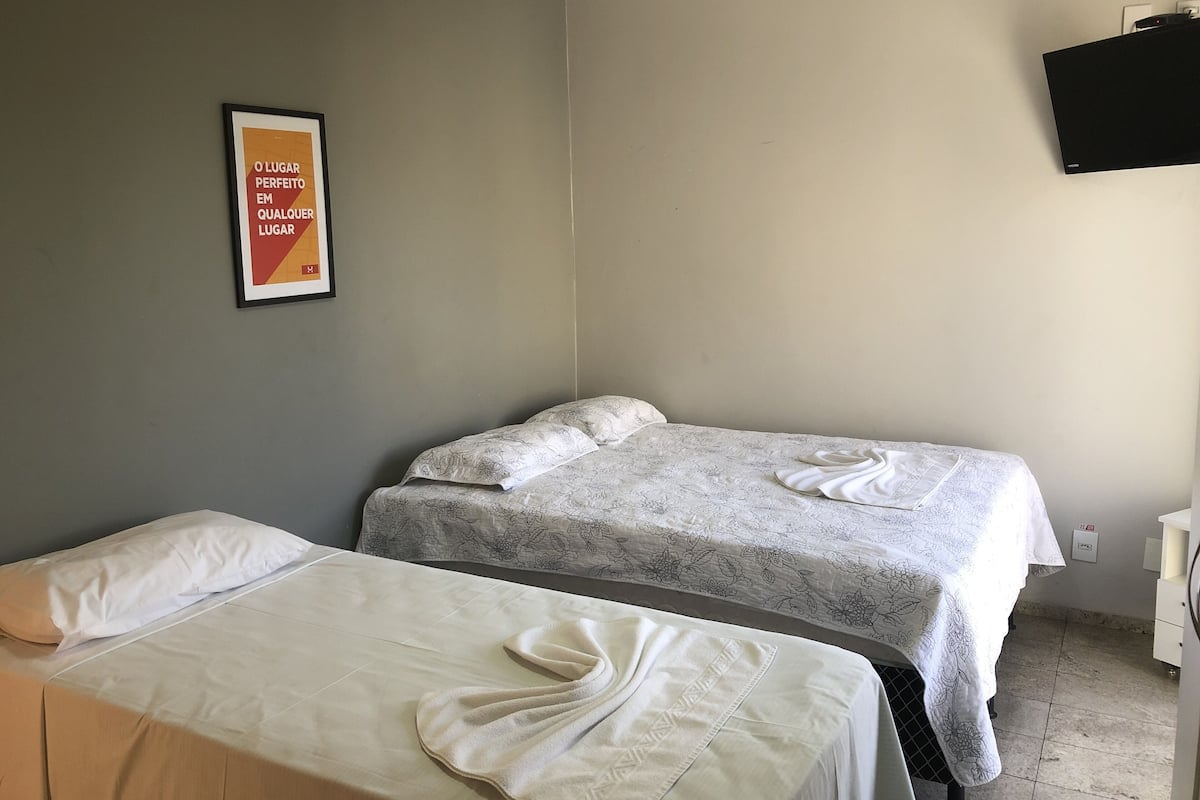 Ein Hotelzimmer mit zwei Betten, einem gerahmten Poster an der Wand und einem an der Wand befestigten Flachbildfernseher.