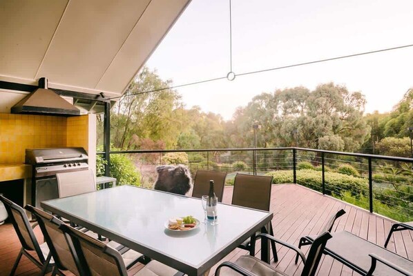 Un espacio de comedor al aire libre con una parrilla, una mesa y sillas, con vistas a un paisaje boscoso.