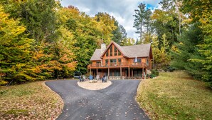 A log cabin with a porch and outdoor seating area, surrounded by trees and a curved driveway.