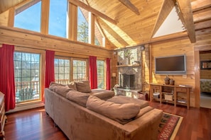 A log cabin interior with a large sofa, stone fireplace, and a TV mounted on the wall. - New listing - Beautiful Spacious Custom Log Cabin. (Way Bartlett)