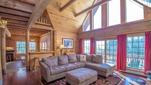 A spacious living room with a large sectional sofa, wooden beams, and large windows.