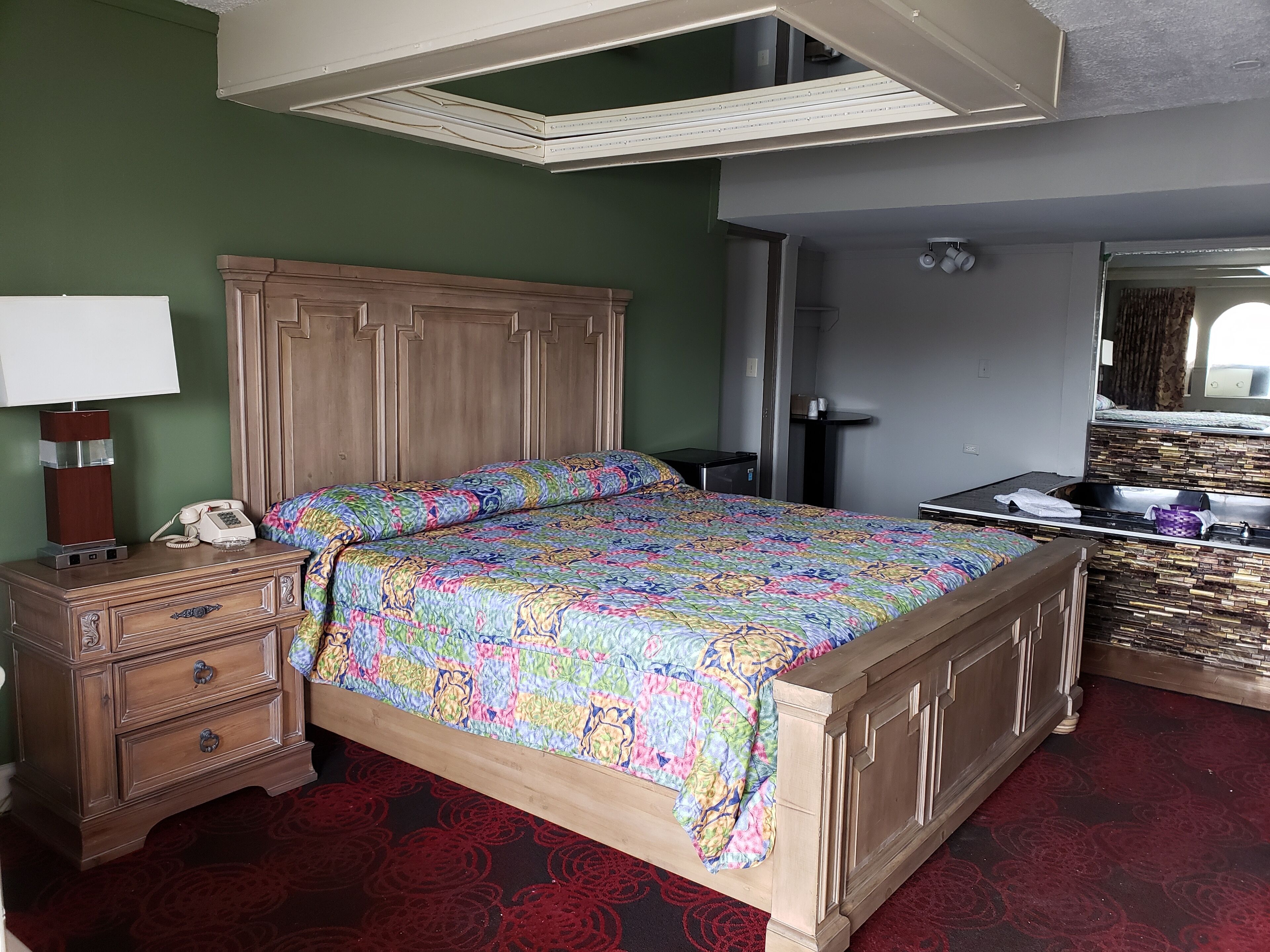 A bedroom with a wooden bed, a nightstand with a lamp, a dresser, and a mirror.