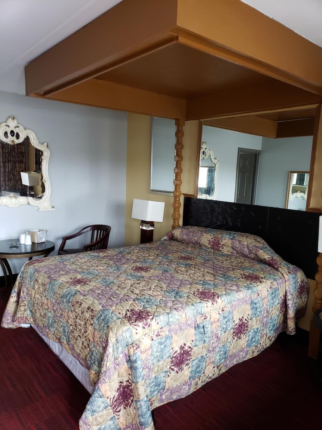 A hotel room with a large bed, a desk with a chair, a lamp, and a mirror on the wall.