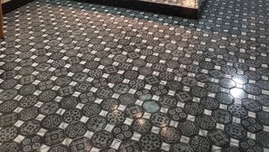 A room with a patterned floor, a desk with a computer, a chair, and a glass partition.