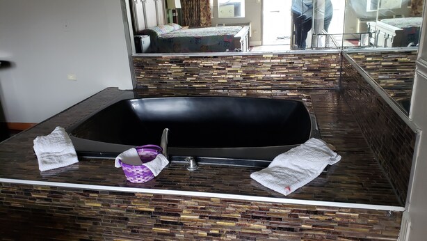 A bathroom with a stone-patterned vanity, a black bathtub, and towels.