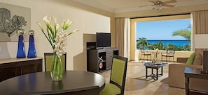 Ein Hotelzimmer mit Esstisch, Stühlen, einem Fernseher und Blick aufs Meer.