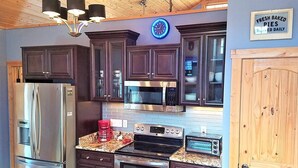 A kitchen with dark wooden cabinets, stainless steel appliances, a red coffee maker, and a sign indicating fresh baked pies. - Blue Pine Lodge  - w/ Hot Tub - What a Mountain Cabin Should Be! (McGaheysville)