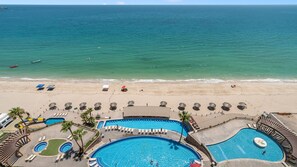 A resort with multiple swimming pools, a beach, and a view of the ocean.