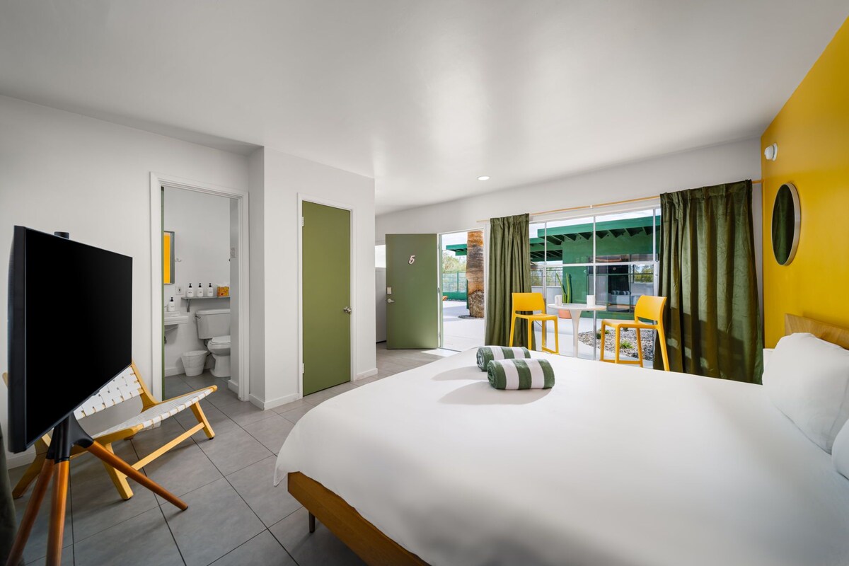 A hotel room with a large bed, a television, a desk with a chair, and a view of the outside.