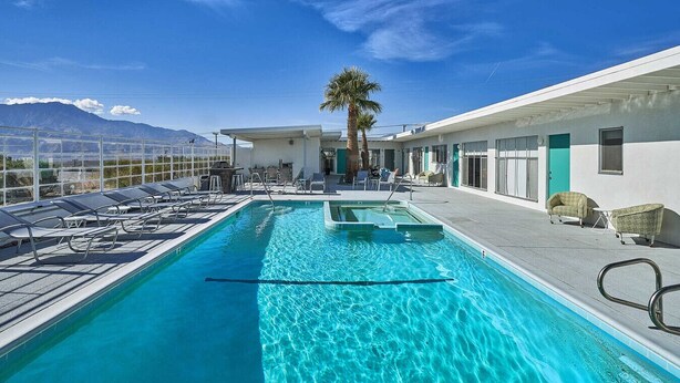 A pool area with lounge chairs, a palm tree, and a view of mountains. - Sagewater Springs - Adult Only (Desert Hot Springs)