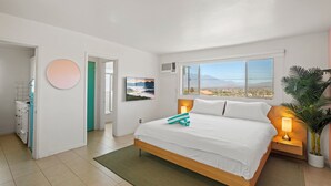 A modern bedroom with a large bed, a view of the city, and a potted plant. - Sagewater Springs - Adult Only (Desert Hot Springs)