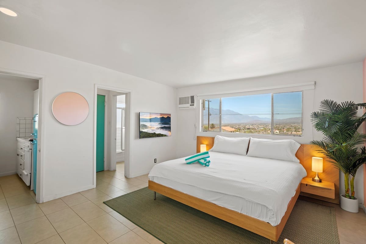 A modern bedroom with a large bed, a view of the city, and a potted plant.