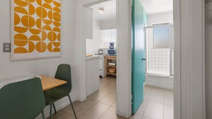 A compact kitchen with a dining area, a blue door leading to a balcony, and a framed artwork on the wall. - Sagewater Springs - Adult Only (Desert Hot Springs)