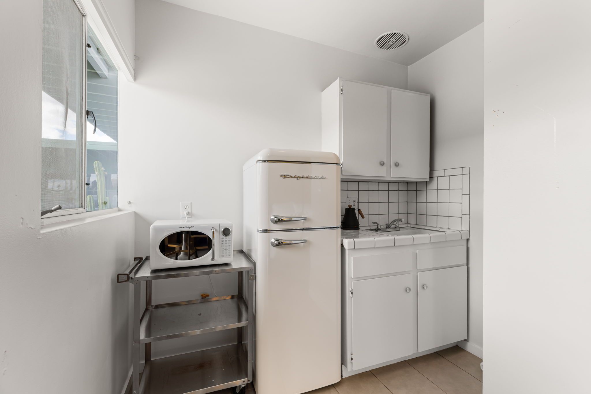 A compact kitchenette with a white refrigerator, a microwave, and a sink.