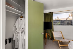 A hotel room with a walk-in closet, a television on a tripod, a chair, and a view of the outdoors. - Sagewater Springs - Adult Only (Desert Hot Springs)