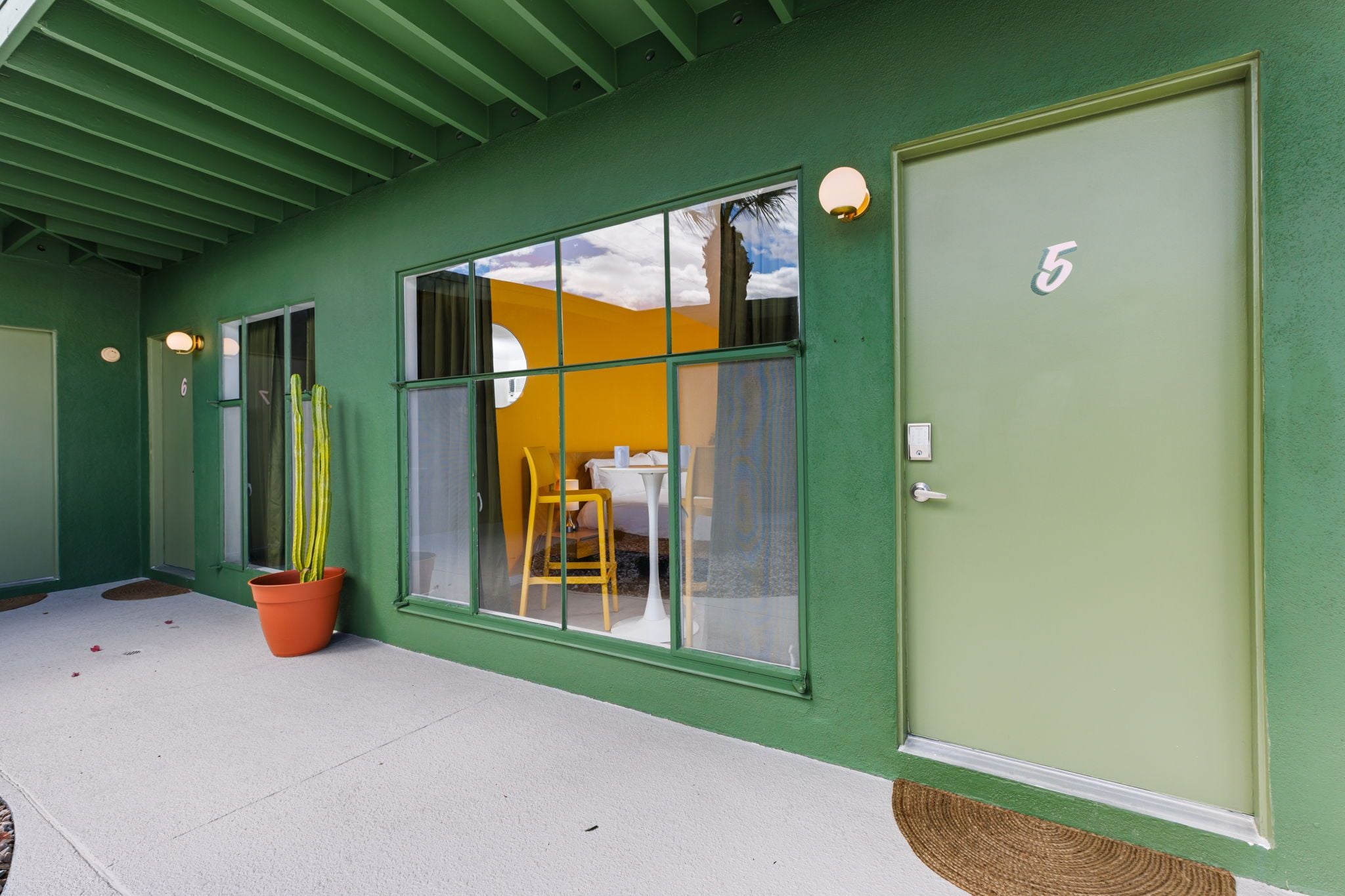 A building with a green exterior, a large window with a view of the sky, and a door marked with the number 5.