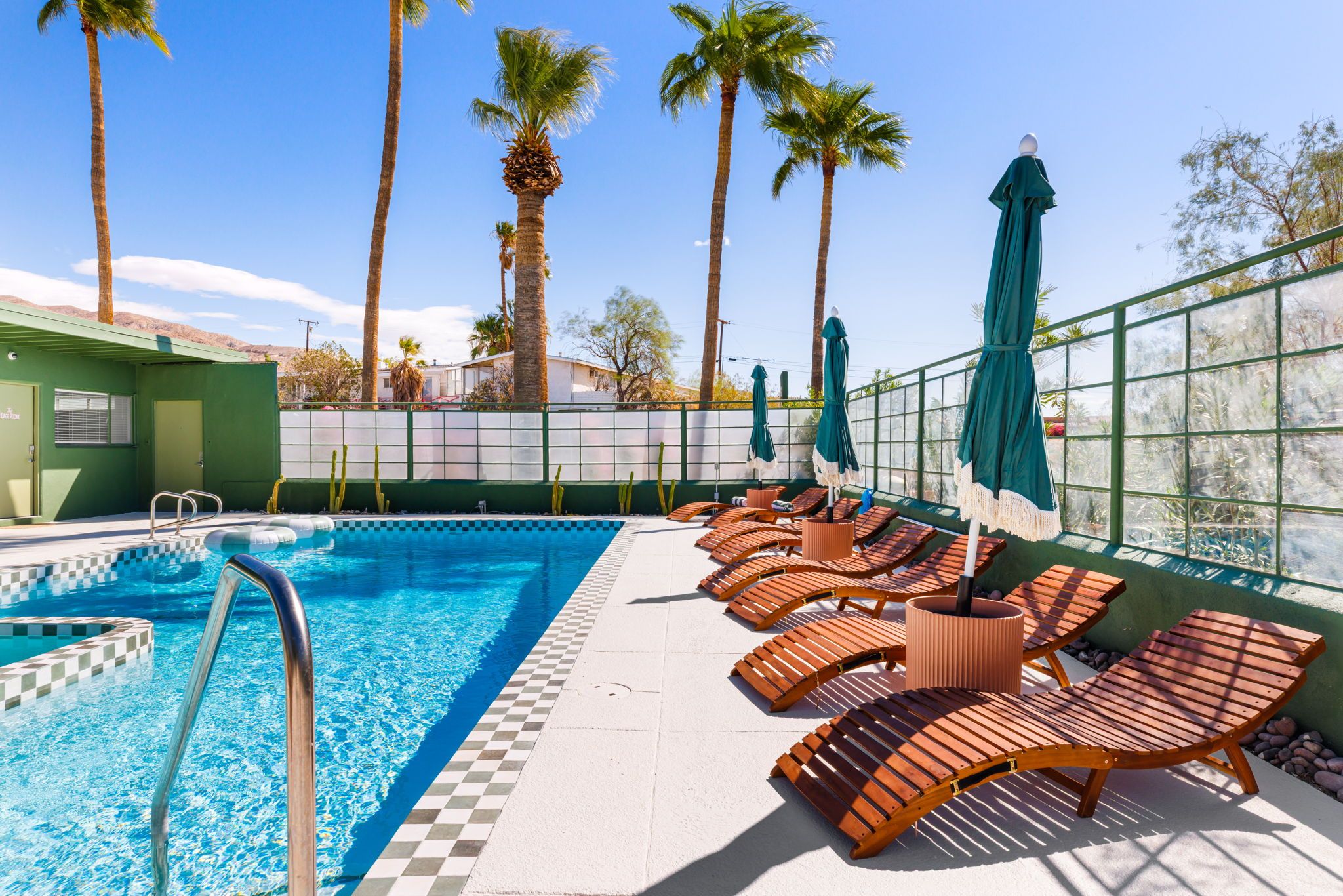 A swimming pool with lounge chairs and umbrellas, surrounded by palm trees.