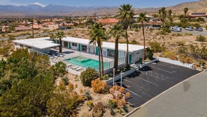 A modern building with a swimming pool, surrounded by desert vegetation and palm trees, with mountains in the background. - Sagewater Springs - Adult Only (Desert Hot Springs)