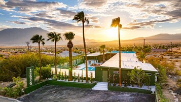 Zona junto a la piscina con vista a la ciudad y montañas, rodeada de palmeras.