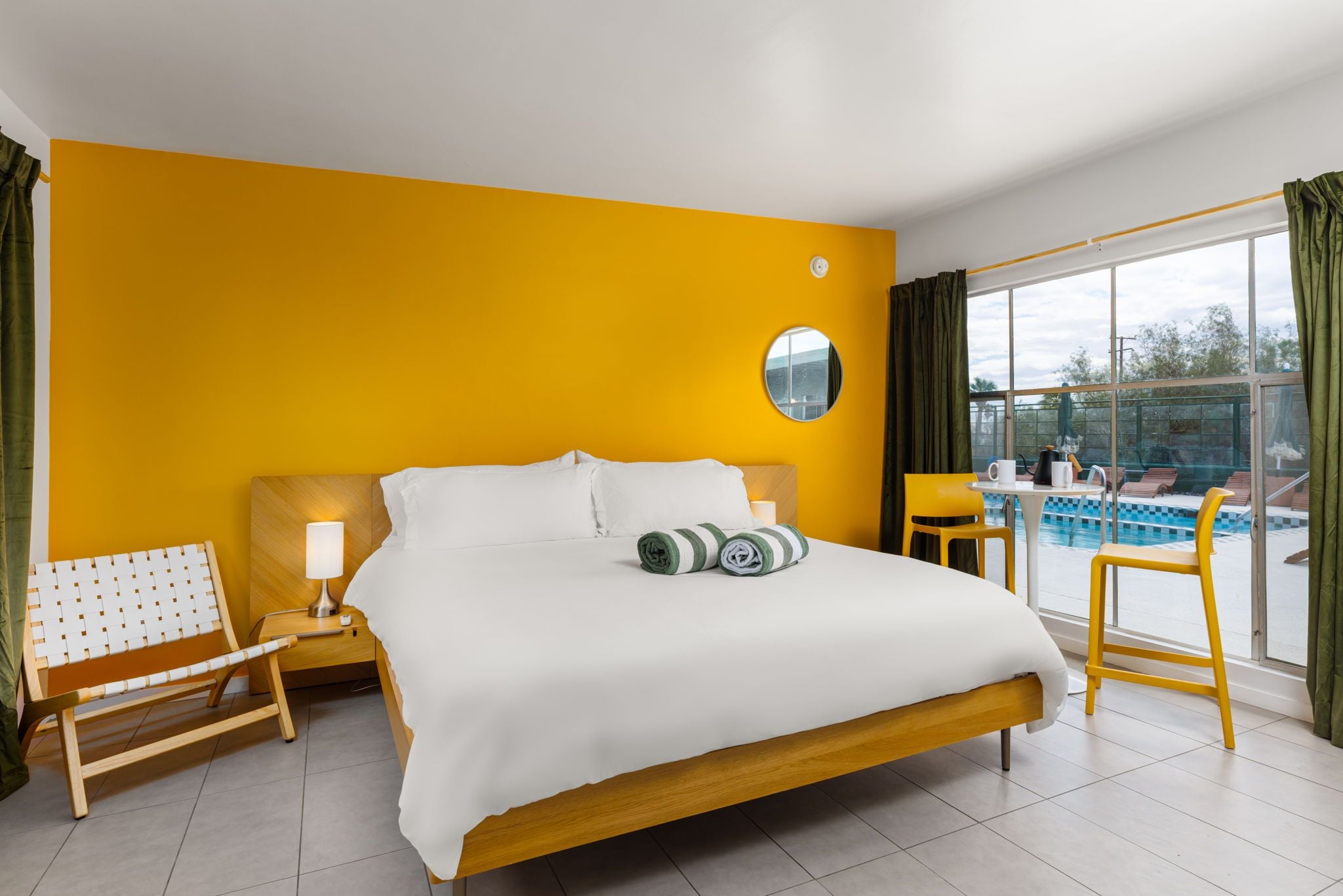 Habitación de hotel con una cama grande, un escritorio, una silla, una mesita y vista a una piscina.