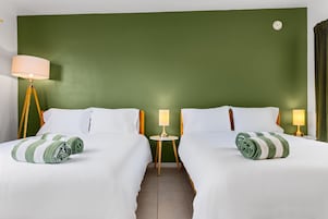 Habitación de hotel con dos camas, paredes verdes y una mesa redonda entre ellas.
