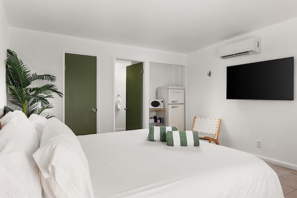 Habitación de hotel con una cama grande, televisor montado en la pared y una pequeña zona de kitchenette.