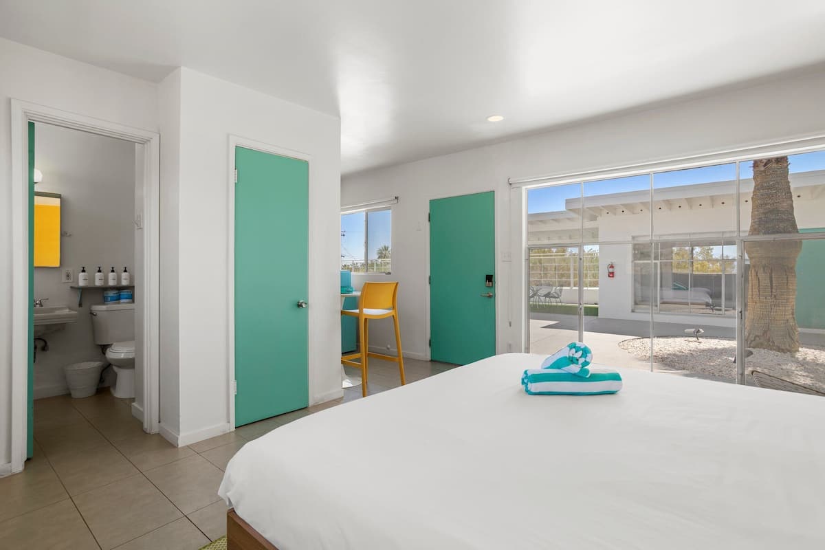 A hotel room with a large bed, a chair, a small table, and a view of the outside.