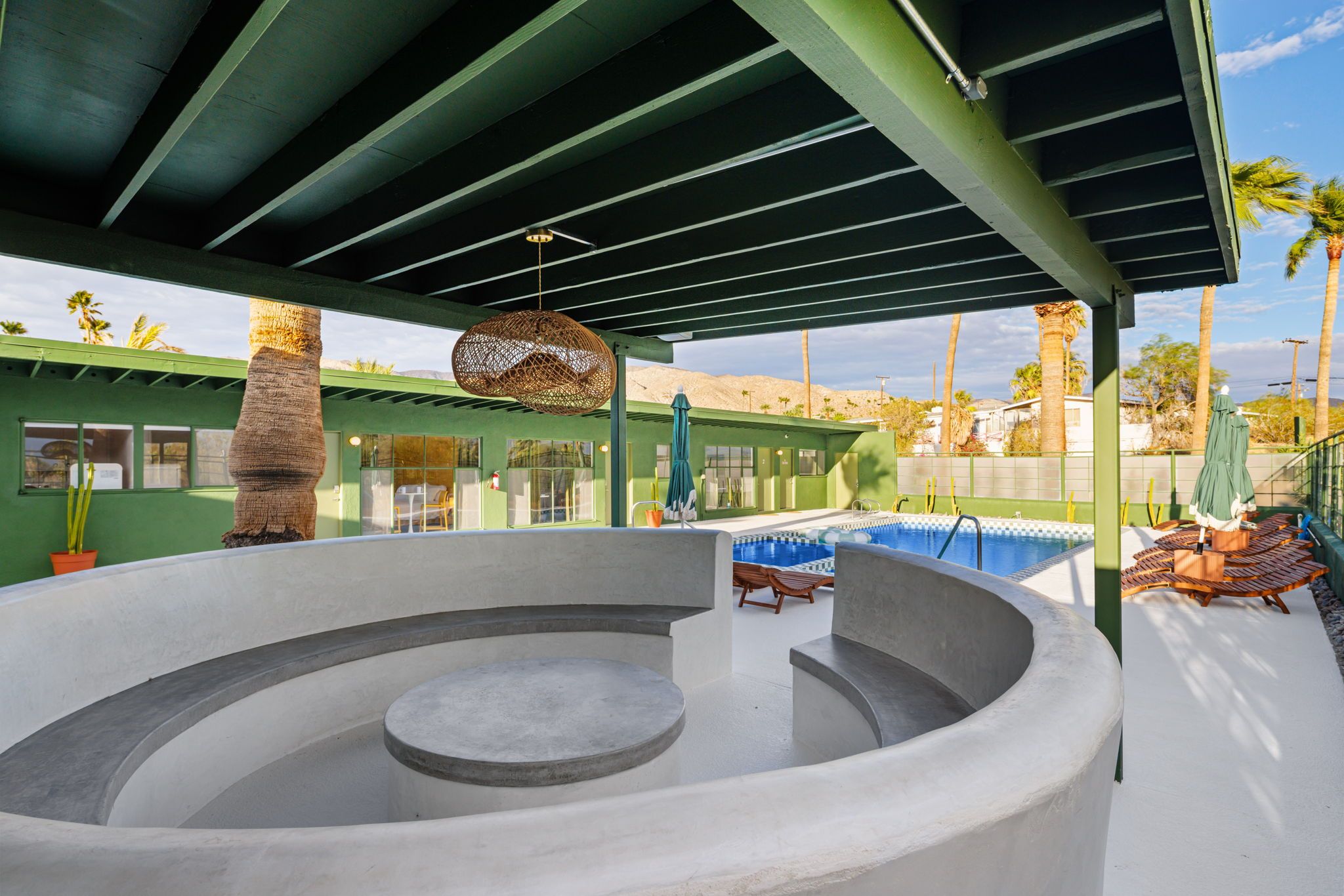 Un jacuzzi circular con piscina aledaña, un área de estar techada y vista a palmeras y montañas al fondo.