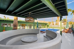 Un jacuzzi circular con piscina aledaña, un área de estar techada y vista a palmeras y montañas al fondo.