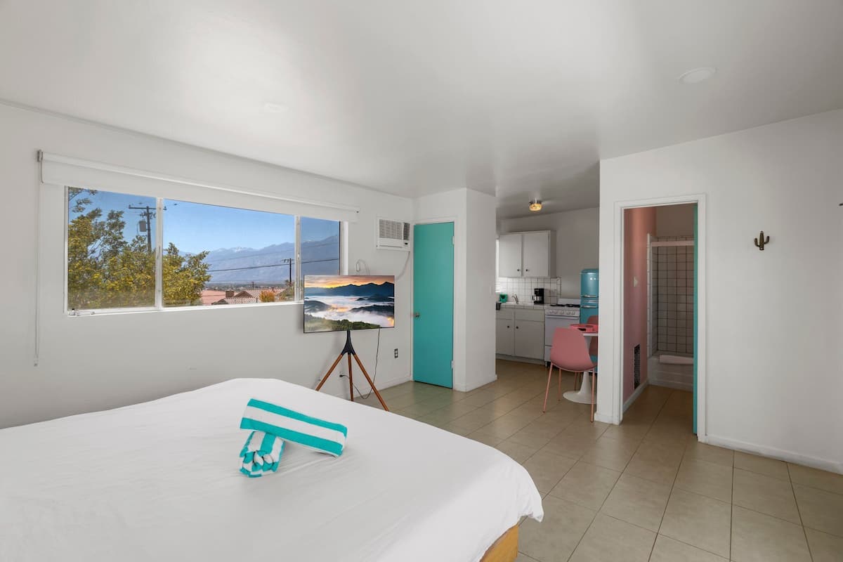 A bedroom with a bed, a painting, and a view of mountains through the window.