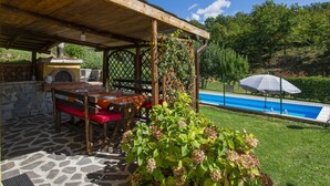 Une terrasse extérieure avec un sol en pierre, des meubles en bois et un four en briques.
