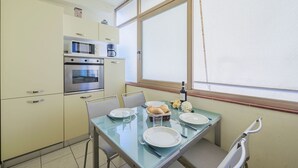A compact kitchen with a microwave, oven, and coffee maker. There is a dining table with plates, glasses, and a basket of rolls. - Beautiful apartment for 5 guests with A/C, TV and balcony (Camaiore)