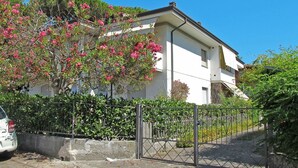 A two-story building with a white facade, a gated entrance, and a tree with pink flowers in front. - Beautiful apartment for 5 guests with A/C, TV and balcony (Camaiore)