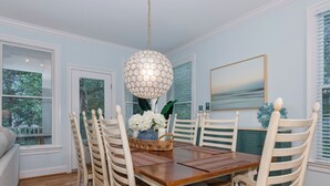 Un comedor con una mesa de madera, sillas blancas, una lámpara colgante y un florero con flores.