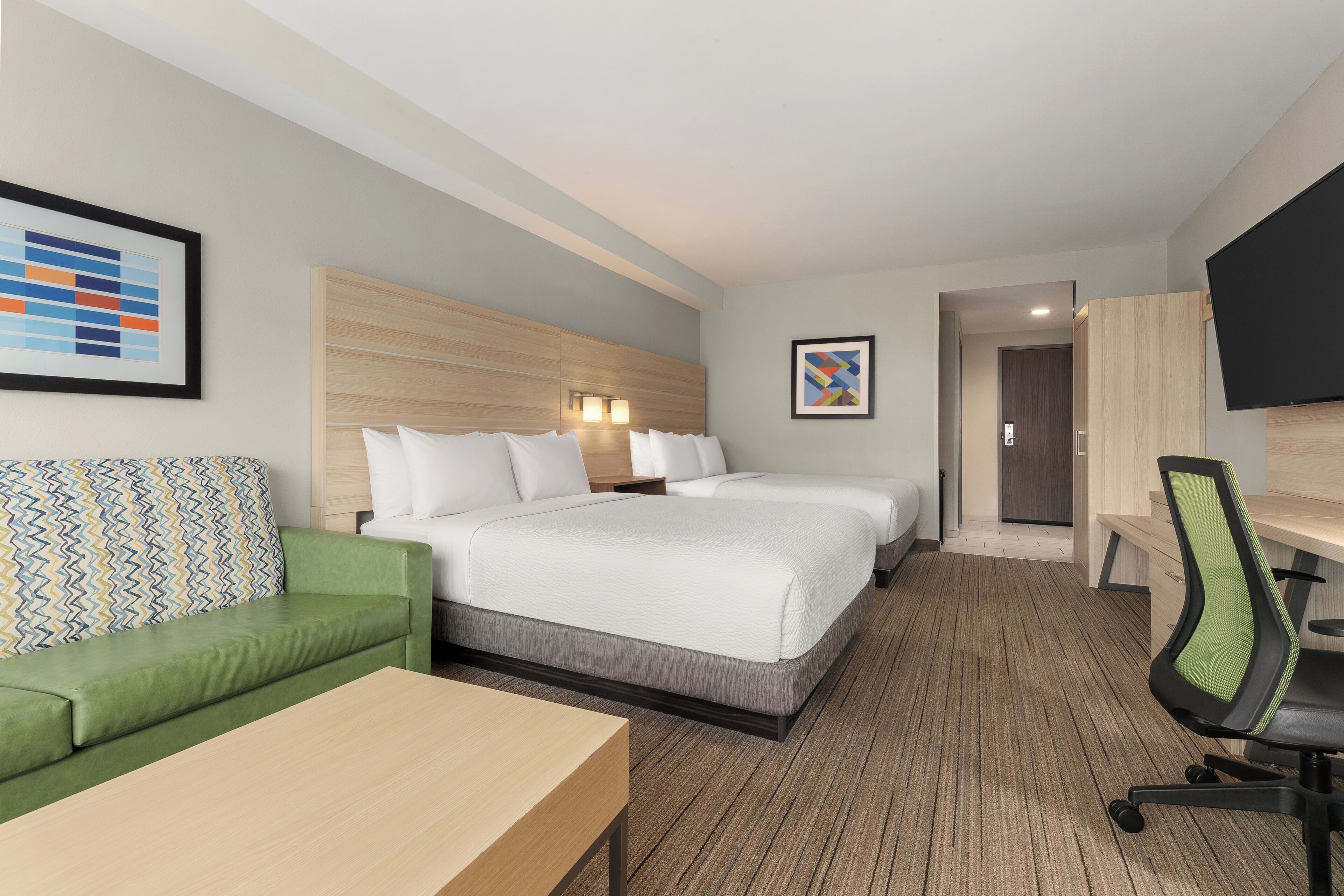 Ein Hotelzimmer mit einem Bett, einem grünen Sofa, einem Schreibtisch und einem Fernseher.