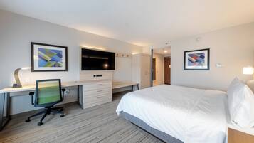 A hotel room with a bed, a desk with a chair, a flat-screen TV, and artwork on the walls.