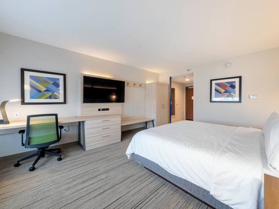 Quarto de hotel com cama, escrivaninha com cadeira, TV de tela plana e obras de arte nas paredes.