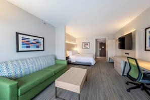 Habitación de hotel con un sofá verde, una cama, un escritorio con una silla y un televisor montado en la pared.