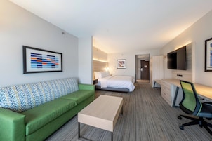 A hotel room with a green sofa, a bed, a desk with a chair, and a TV mounted on the wall.