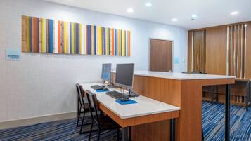 Un centre d’affaires équipé d’une grande table, de chaises, d’ordinateurs et agrémenté d’une œuvre d’art murale aux couleurs vives.