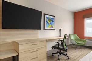 Un espacio de oficina moderno con un televisor de pantalla plana, un cuadro abstracto enmarcado, un escritorio de madera con cajones, una silla de oficina verde y un radiador.
