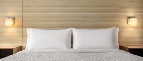 Una habitación de hotel con cabecera de madera, dos lámparas de noche y una cama bien hecha.