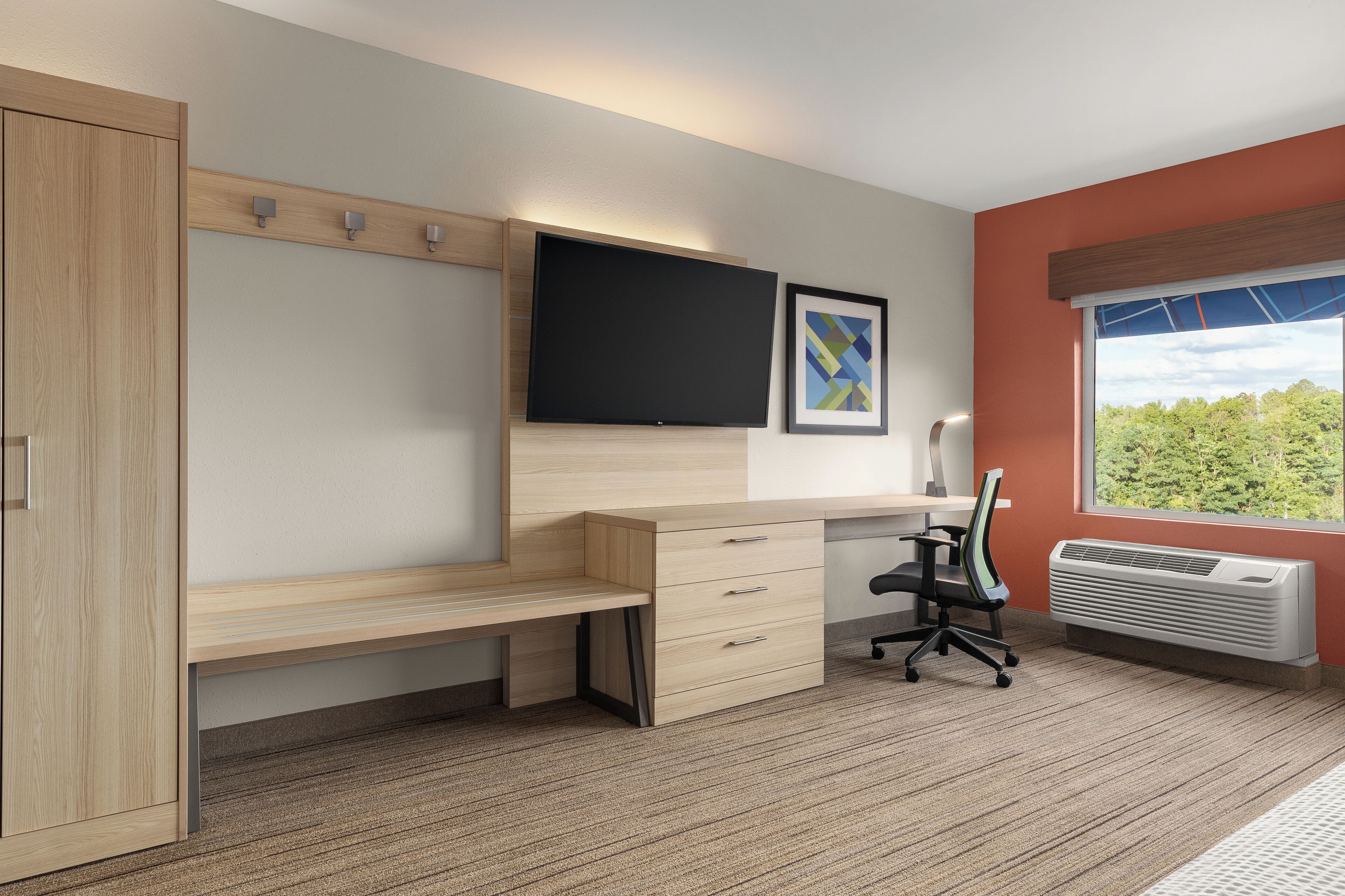 A modern bedroom with a wooden desk, a flat-screen TV, a framed picture, and a window with a view.