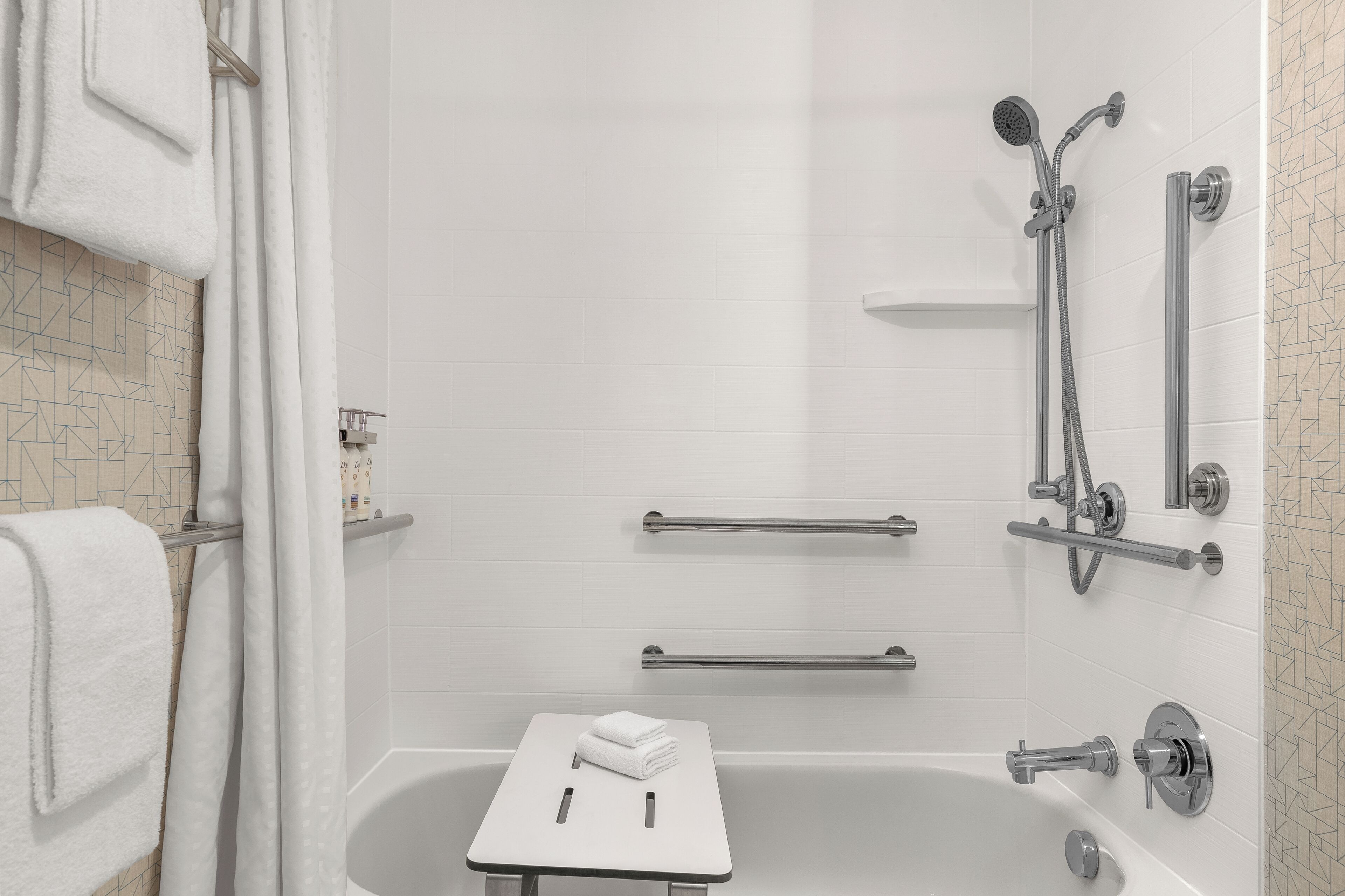 A modern bathroom with a walk-in shower, grab bars, a towel rack, and a small table with a towel.