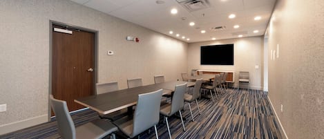 A conference room with a large table, chairs, a projector screen, and a carpeted floor.