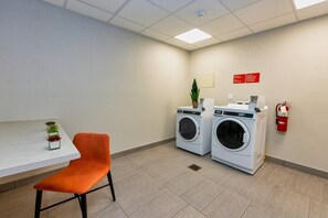 A laundry room with two washing machines, a fire extinguisher, a small table with a potted plant, and an orange chair. - avid hotel Denver Airport Area by IHG (Denver)